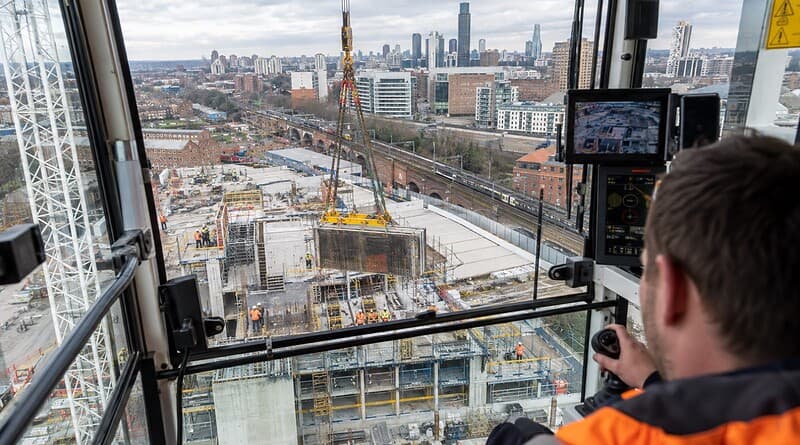 Crane operator in a hi-vis jacket lifting a concrete panel over a high-rise building site