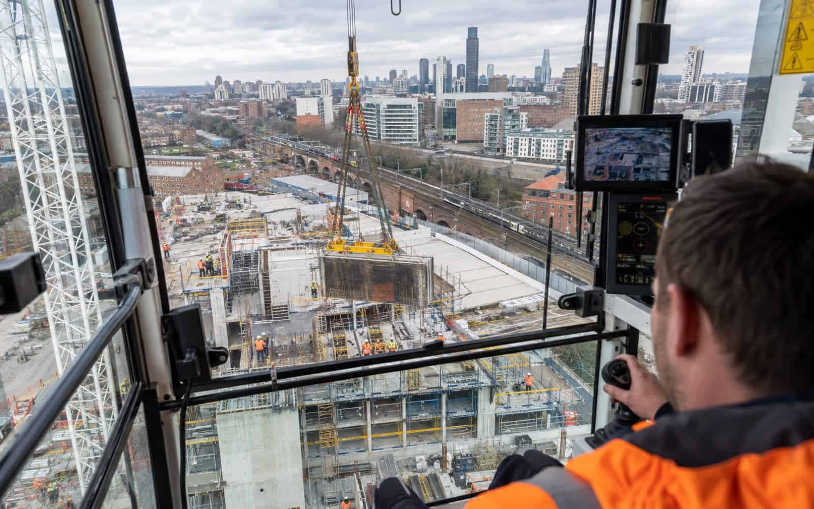 Crane operator in a hi-vis jacket lifting a concrete panel over a high-rise building site