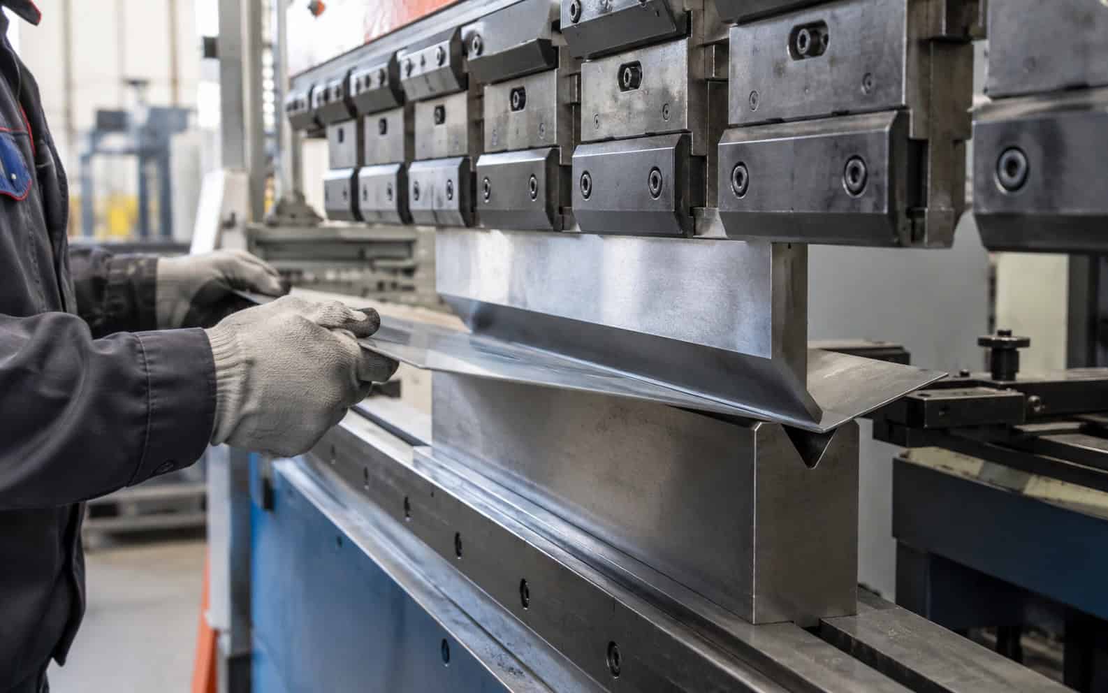 Gloved hands feeding a steel sheet into a press brake as it bends the metal