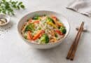Bowl of clear konjac noodles with broccoli, peppers and carrot, with chopsticks beside it