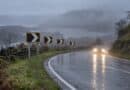 Chevron signs on a wet, misty hill road bend with a car approaching, headlights on