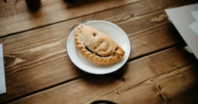 Golden baked pasty with a crimped edge on a white enamel plate on a wooden table