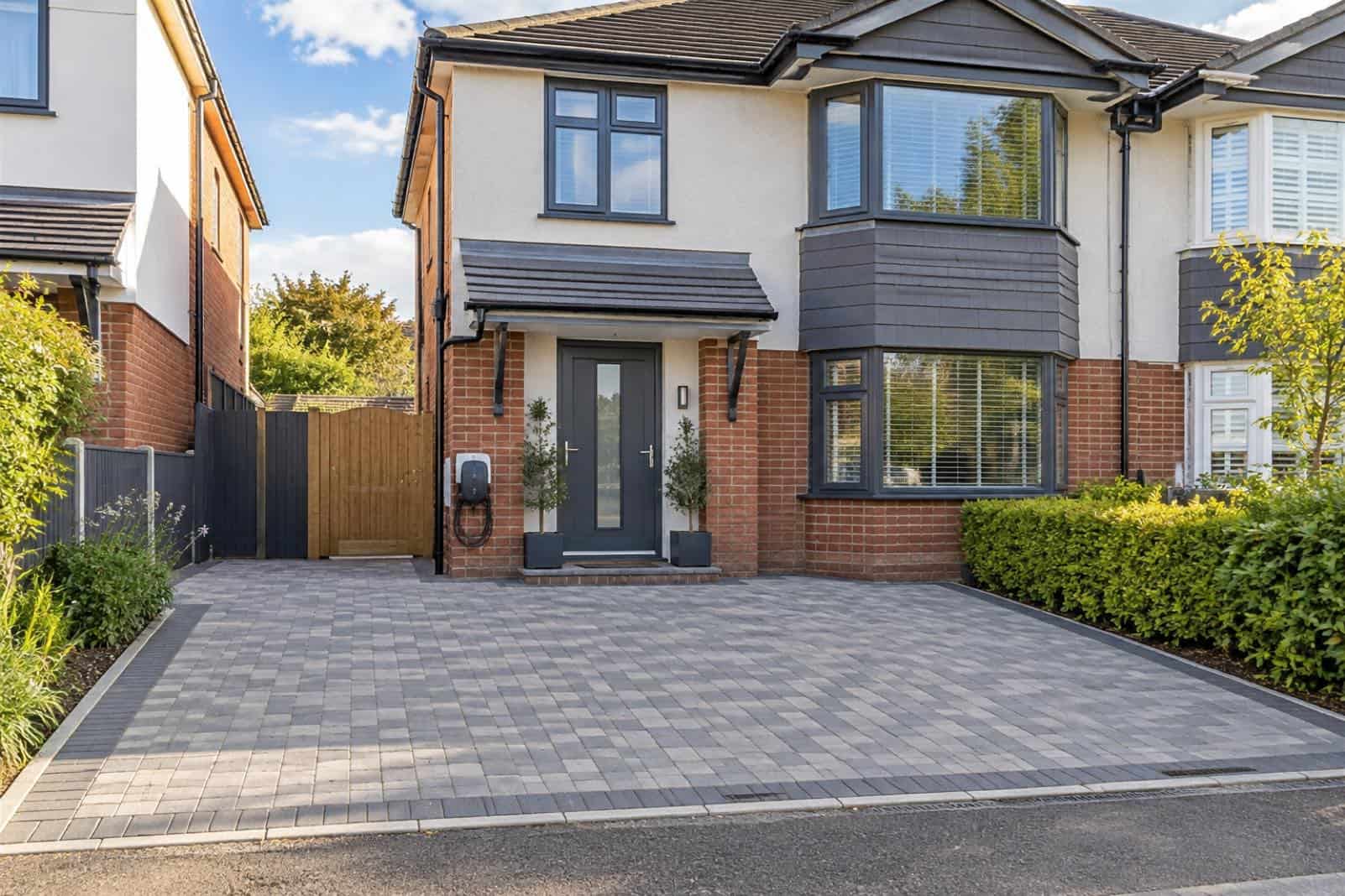 Grey block-paved driveway in front of a semi-detached house with an EV charger by the door