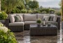 Rain-spotted grey cushions on a rattan corner sofa on a wet stone garden patio