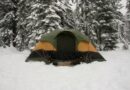 Large green and orange family tent pitched in deep snow among snow-covered pine trees