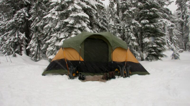 Large green and orange family tent pitched in deep snow among snow-covered pine trees