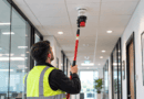 Engineer in a hi-vis vest testing a ceiling smoke detector with a red pole tester