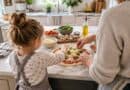Young girl and an adult making a pizza together on a marble kitchen island