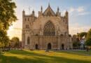 Gothic cathedral west front with a large tracery window in low sunlight, people sitting on the lawn in front