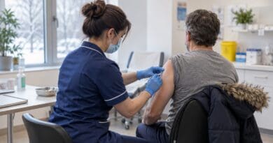 Nurse in gloves and a face mask giving a man a vaccination in his upper arm at a clinic
