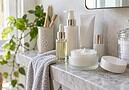 Open jar of moisturiser, facial oil and skincare bottles on a marble bathroom shelf