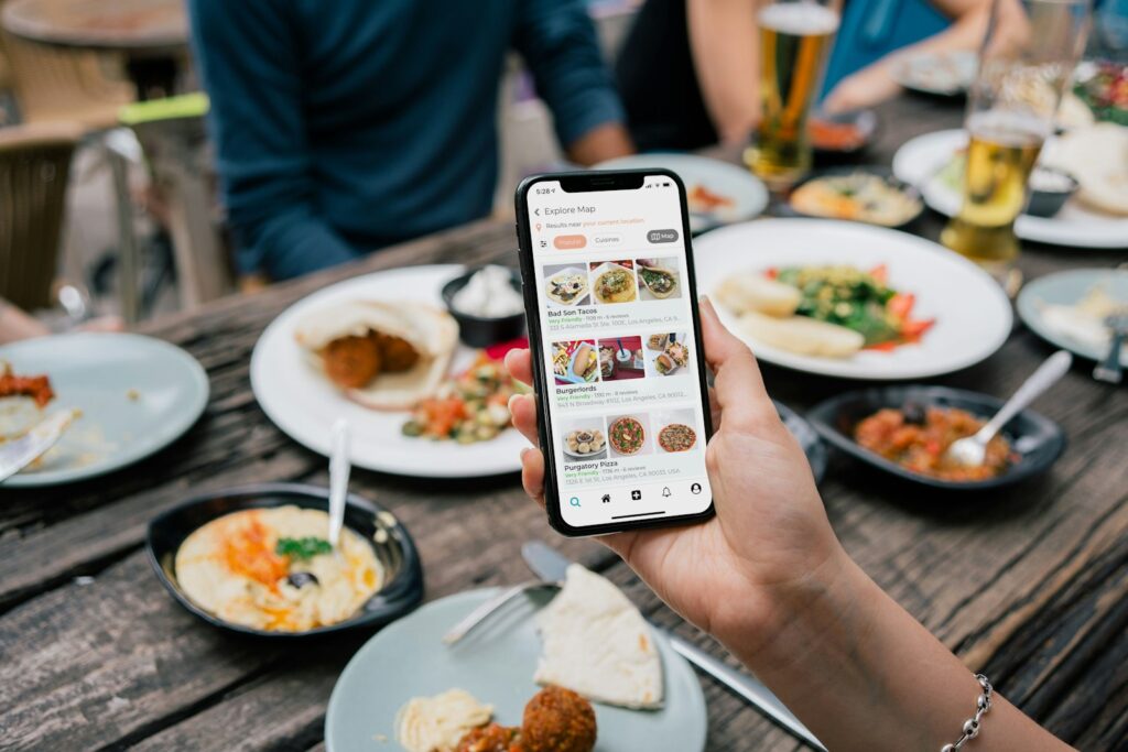 Hand holding a smartphone showing a food menu app above a table of shared dishes at a restaurant