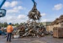 Crane grab dropping scrap metal onto a large pile while a worker in hi-vis watches