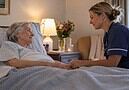 Nurse holding the hand of a smiling older woman lying in bed
