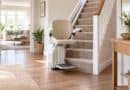 Cream stairlift at the bottom of a carpeted staircase in a bright hallway with wooden floors